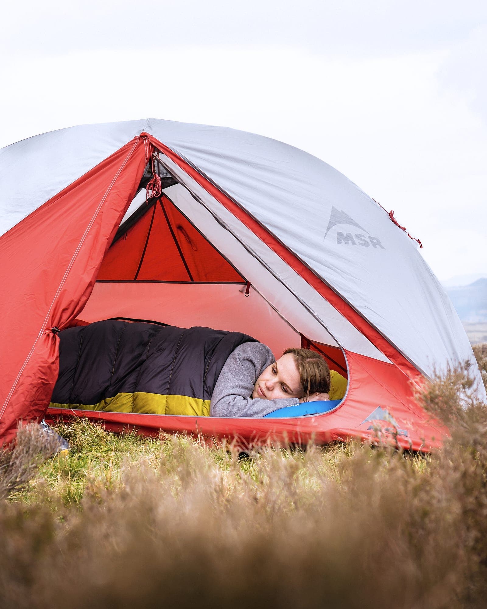 A camper asleep in a tent on a camping mat with a sleeping bag