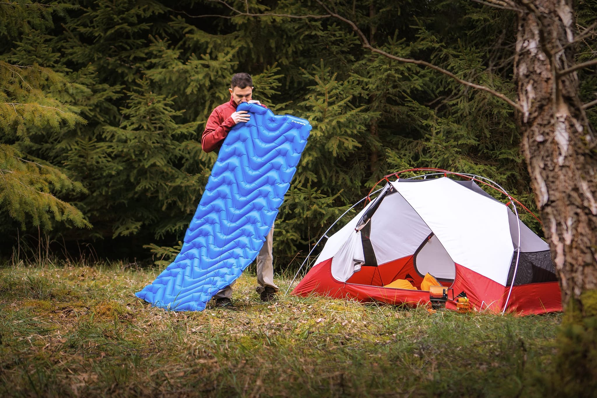 A camper unrolling a camping mat beside a tent below a Peak District plantation