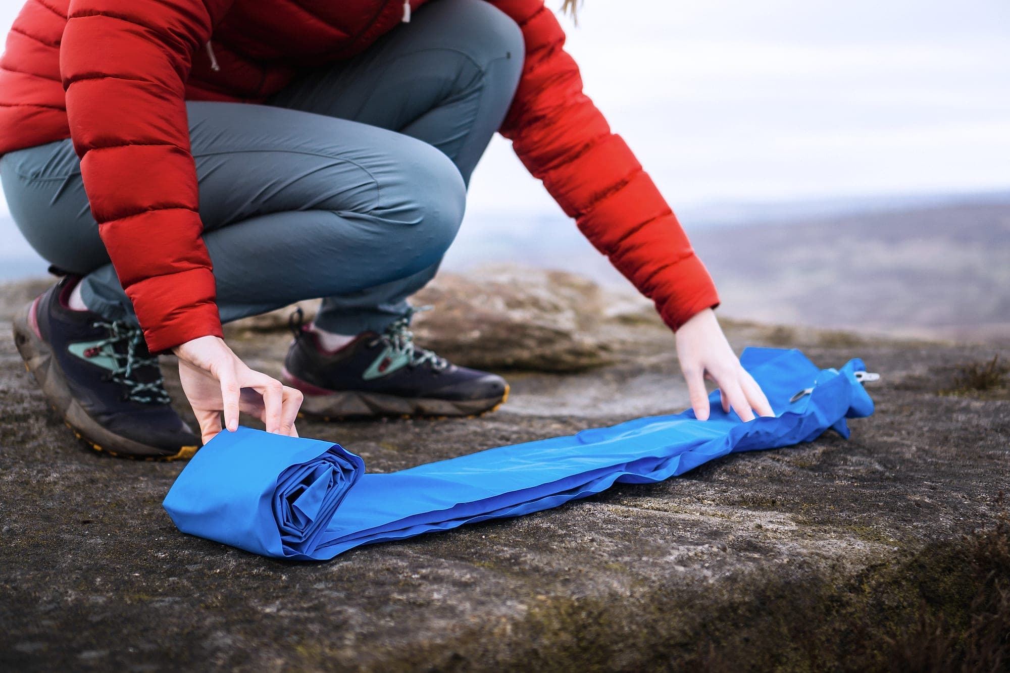 A camping mat being rolled tightly on a gritstone slab ready for packing