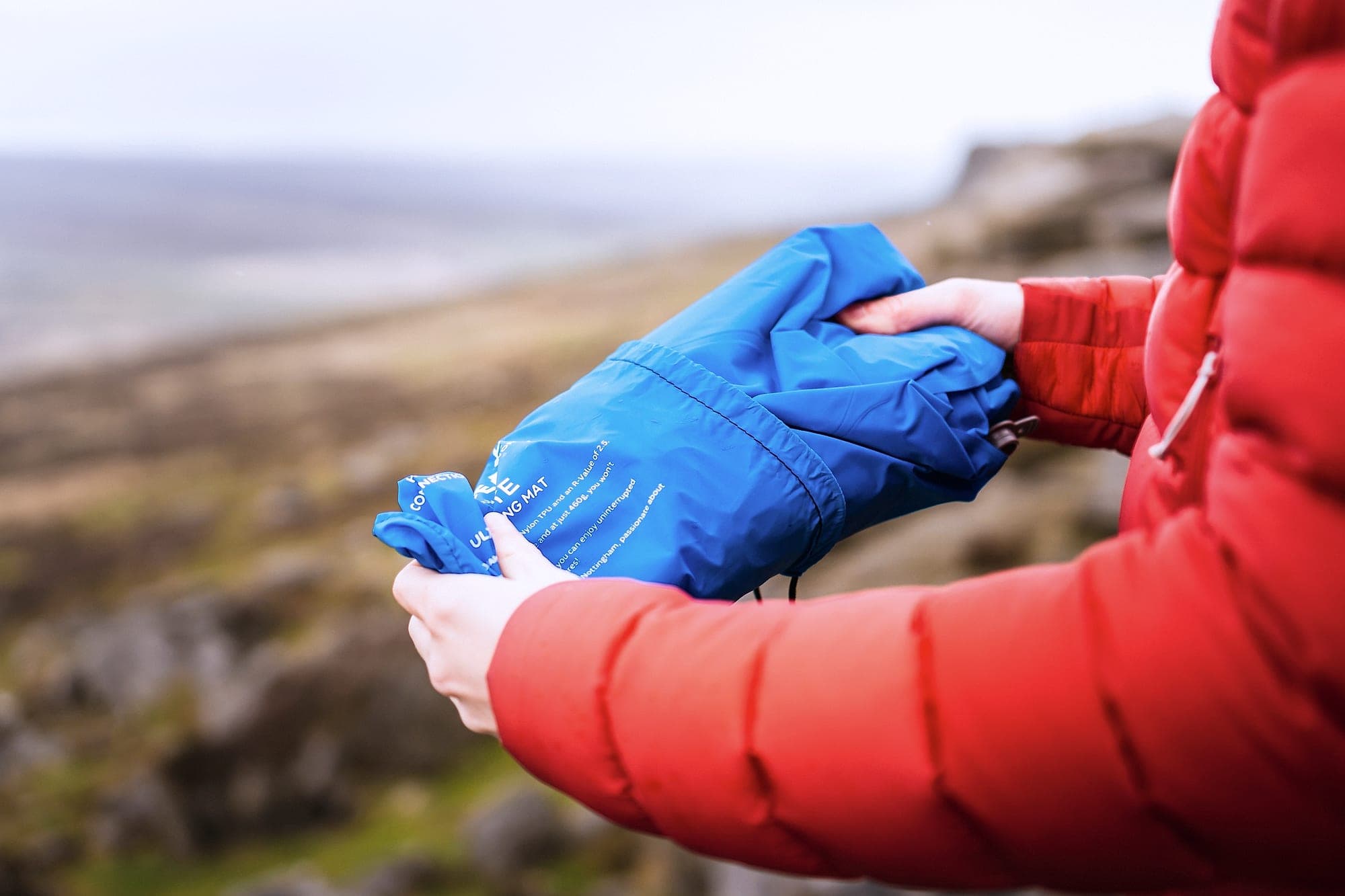 The DreamLite packed into its stuff sack, held in two hands above the valley