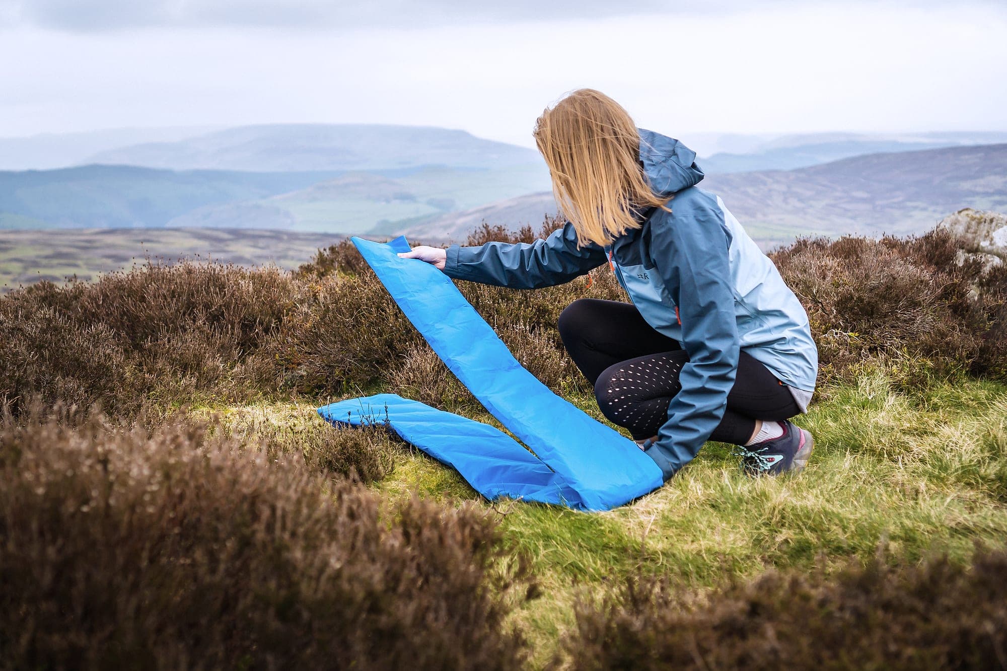 A rambler unrolling the DreamLite on heather moorland above a wide Peak District valley